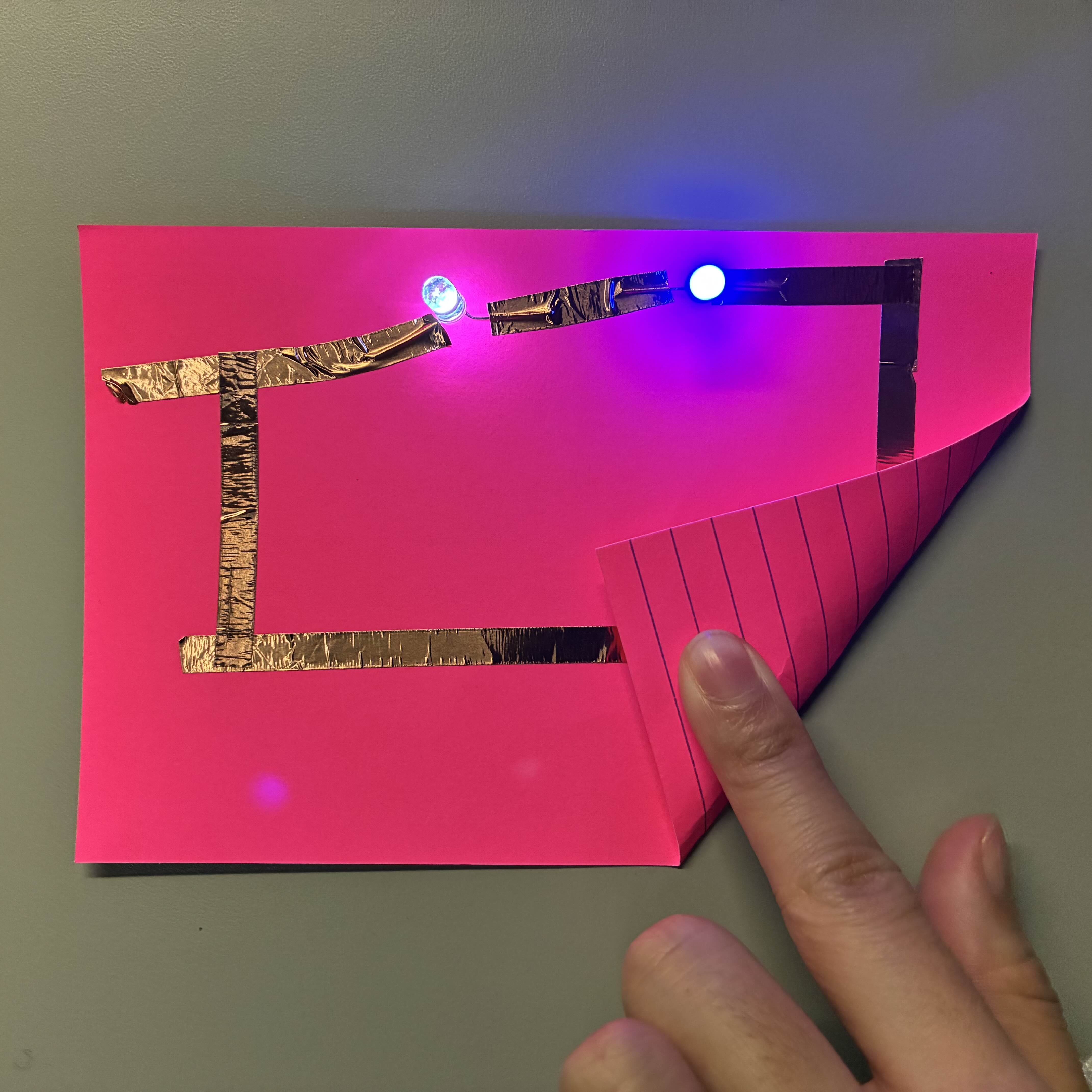 This is my series circuit with the batteries connecting the copper tape to make both the lights turn on at the same time. I used blue and white lights to contrast the pink background.