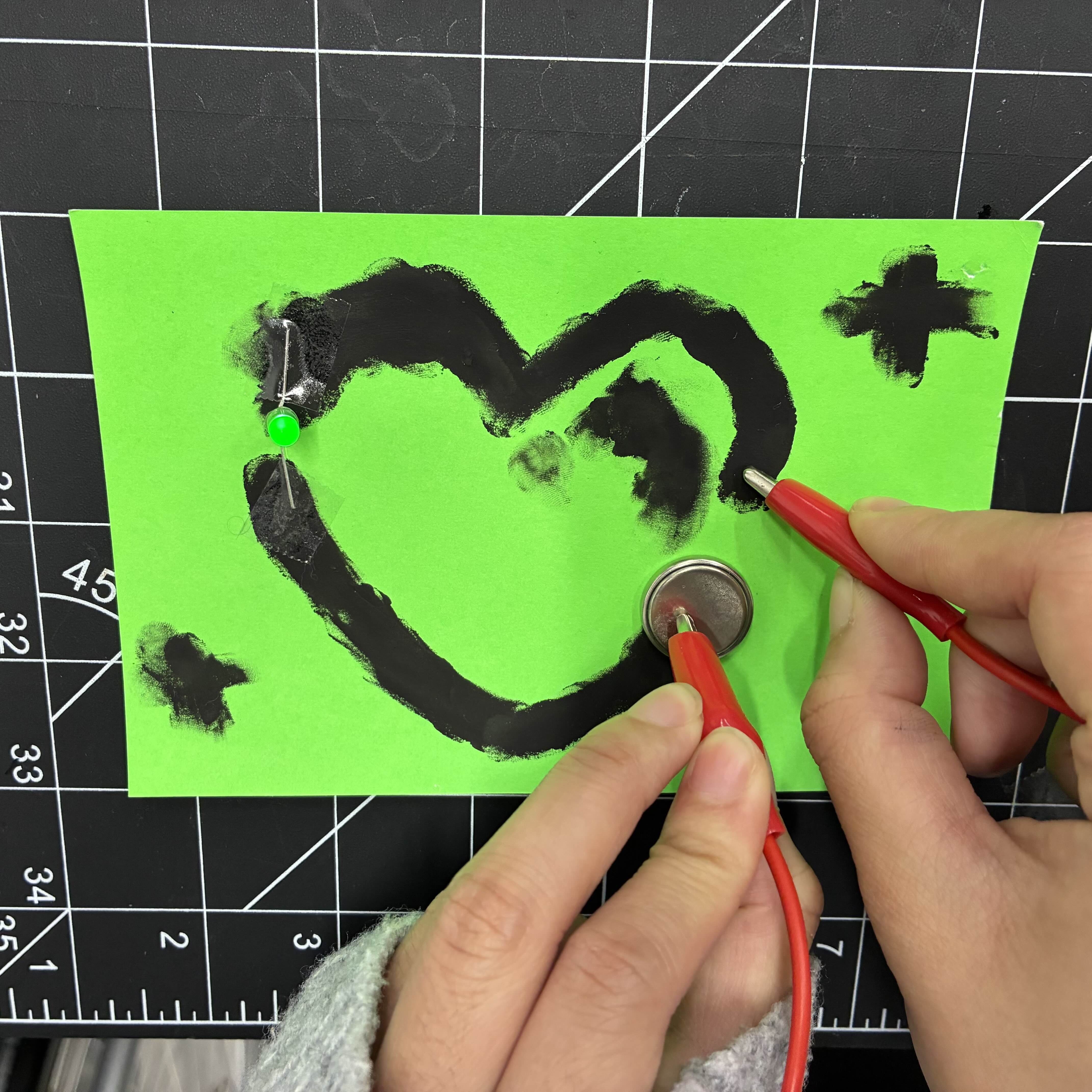 This is the heart made of conductive paint up close to exmplify the glow of the light. I taped an LED light to fill the gap in the heart and then placed a battery on the other end. I then used an alligator clip wire to connect these items together so the light can glow.