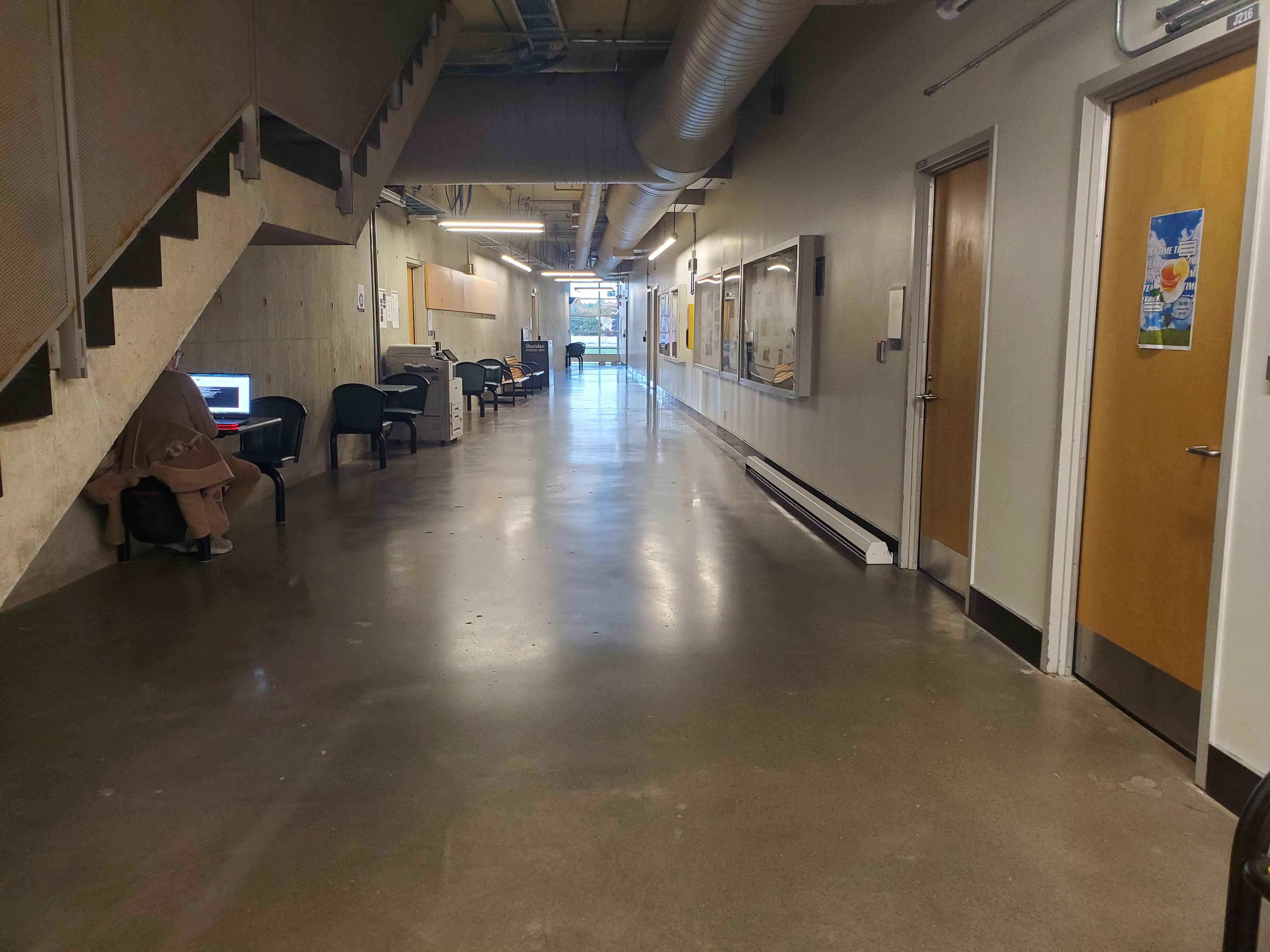 The J-wing second floor has a very brutalist design, the floor, stair, walls, and ceilings are all concrete, with the exception of the wooden doors. The doors being wooden creates good contrast between the rest of the space and it has few wooden benches and seating areas with metal chairs and small tables. The J-wing could use wooden flooring in the hallways to prevent fatigue from standing on the concrete floor all day, this would also make it look more like a school rather than a warehouse. Increased seating would also fit in the hallway and make the space more inviting for students as it is currently unwelcoming.