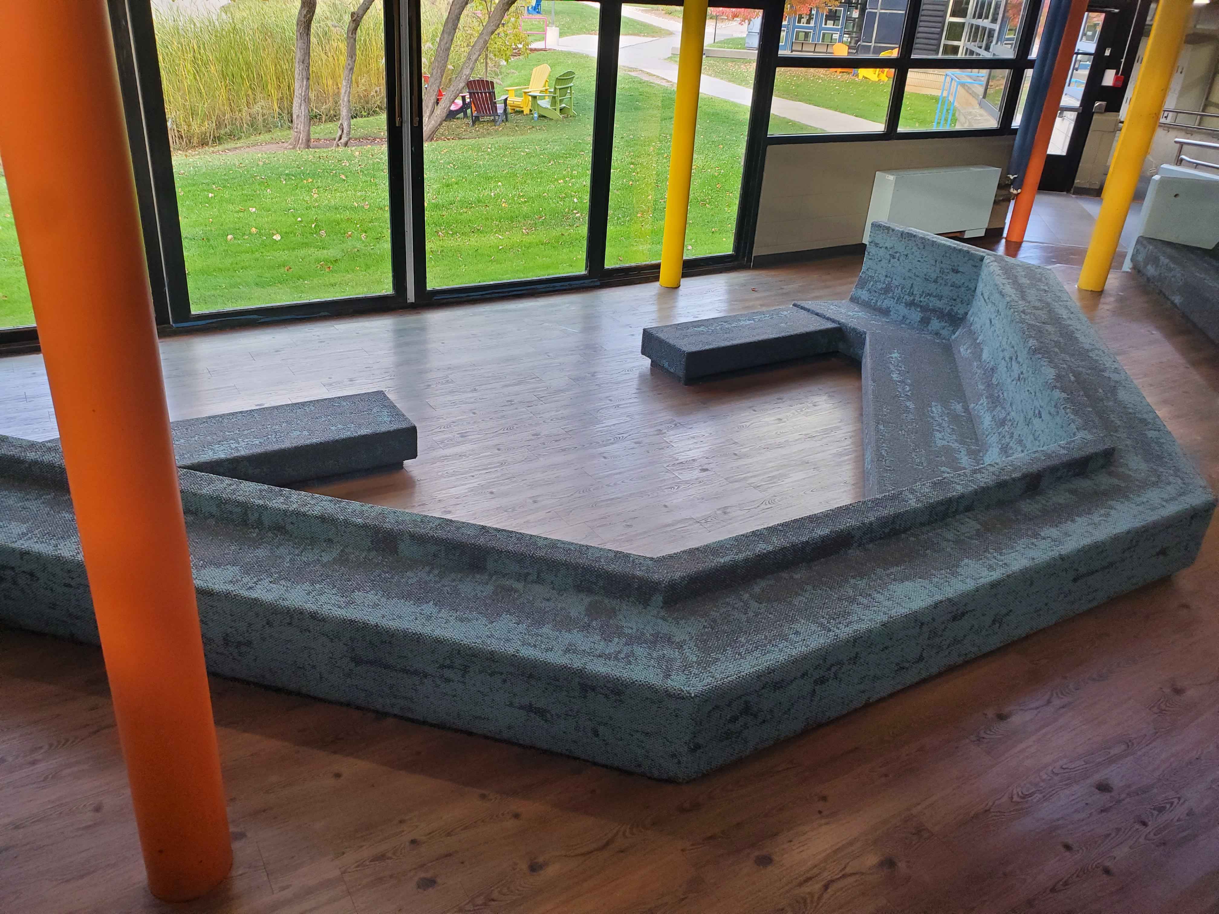 The seating pit in C-wing has wood flooring for a more natural look to contrast the concrete around the area. The beams have colour to brighten up the place but overall the colour is very muted in this area. This area is predominantly used as a pit stop for students to sit or a commercial area for people to sell items. Something to improve this would be adding more cushions to the seating to make it more comfortable for students and add more colours to attract people to the area and brighten up the space. Adding some wood tables to the space can also encourage students to sit there more often.